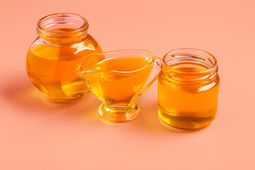 Jars and gravy boat of sweet honey on pink background