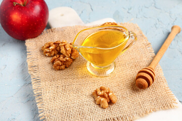 Board with gravy boat of sweet honey, walnut and apple on blue background