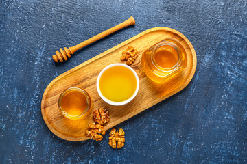 Bowl and jars of sweet honey with walnut on blue background