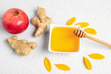 Bowl of sweet honey with ginger, pomegranate and petals on white background