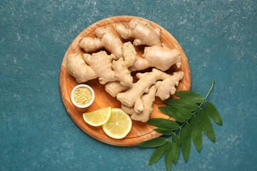 Wooden board with fresh ginger roots, slices of lemon and leaves on blue background