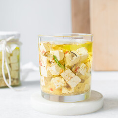 Marinated feta cheese cubes in olive oil in a glass jar. Cheese cubes marinating in olive oil, feta...