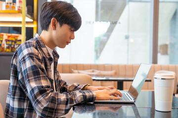 Young Asian man freelancer sitting in cafe in the city working business freelance job on laptop computer and digital tablet. Digital nomad people working from anywhere on gadget device online network.