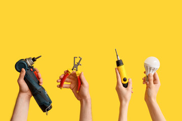 Electrician hands with light bulb and tools on yellow background