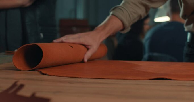 craftsman unroll material on the table , smooth it before sewing process Slow motion Workshop for making leather product for special order. manufacturing industry and footwear production process