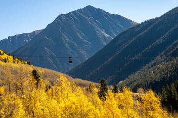 An old ore cart on a tramway suspended above fall aspens with a mountain backdrop. 
