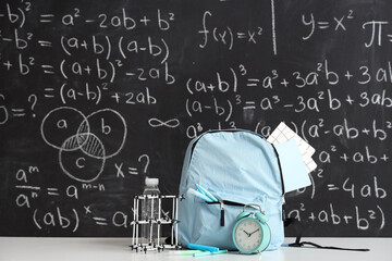 Blue school backpack with stationery, molecular model and bottle of water on white table near black...