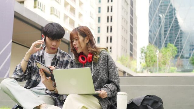 Young Asian man and woman university college student sitting in public park in the city working e-learning class study project or freelance work job on laptop computer and digital tablet together.
