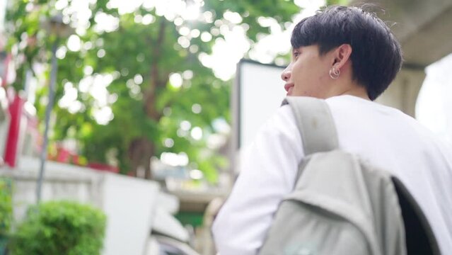 Young Asian man college student with backpack walking city street go to university in the morning. Generation z people enjoy and fun university life. Education back to school and city life concept.