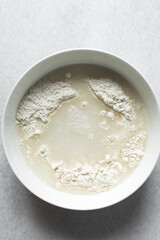 Water and flour in a white bowl, hydrating flour before baking, autolyse process of baking bread