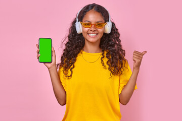 Young happy Indian woman teenager in wireless headphones holding mobile phone and smiling looking...