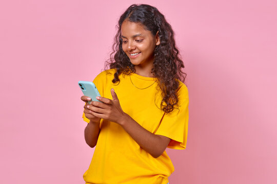 Young Cheerful Indian Woman With Black Hair Holding Phone Using Mobile Apps For Shopping And Ordering Cheap Goods With Targeted Delivery Stands On Pink Background. Discounts, Promotions, Cashback