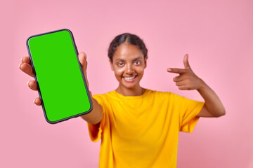 Young satisfied beautiful Indian woman smiling pointing finger at mobile phone with green screen...