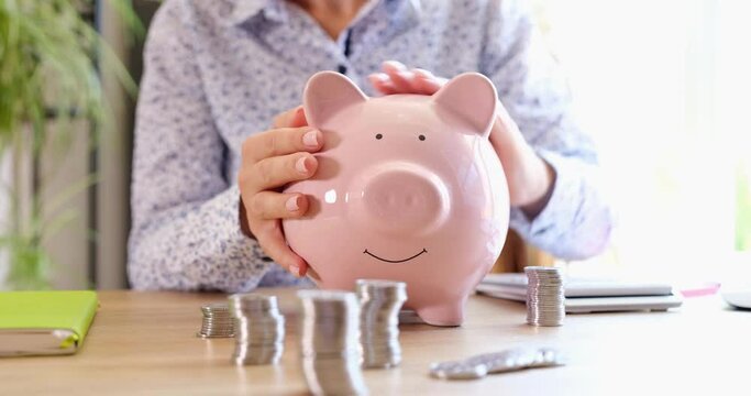 A woman sitting in the office strokes a pink piggy bank, a closeup, shallow focus. Saving money, coins