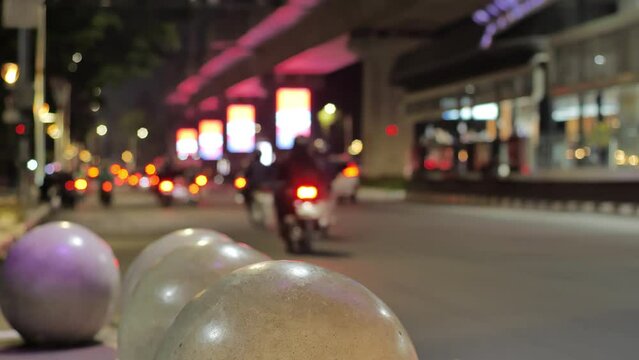  Motorcycles and cars walking past one of the Trans Jakarta bus stops at night. Shot with background blur and focus on the round seat. Medium shot and handheld.