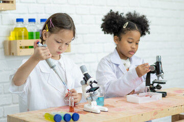 Two cute little girl student child learning research and doing a chemical experiment while making analyzing and mixing liquid in test tube at science class on the table
