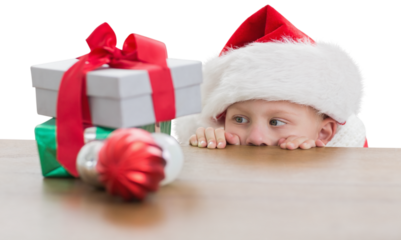 Digital png photo of caucasian boy in santa hat looking at christmas gifts on transparent background