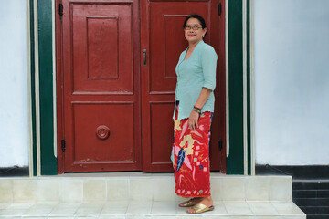 Javanese adult woman in her local dress, standing on staircase of an entrance door to her...