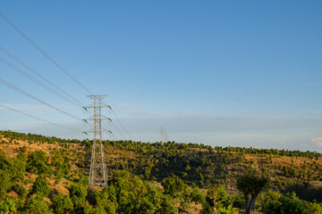 Landscape of hill with High voltage poles standing in a field under a blue sky, electric...