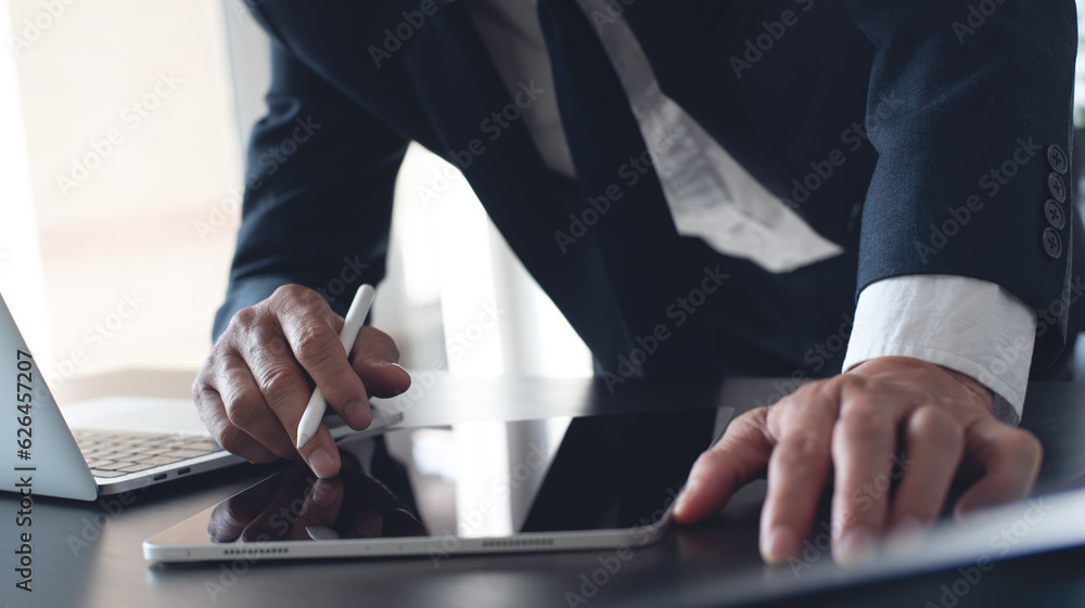 Poster businessman using digital tablet surfing the internet and working on laptop computer on office desk.