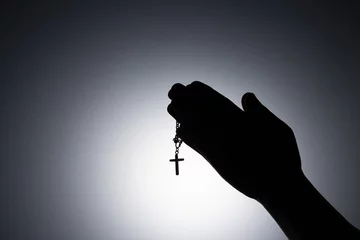 Tuinposter Praying hands holding a rosary, Close up holding necklace with cross, pray for god in the dark, religious Christian symbol with copy space background. God and Spiritual Concepts. © doidam10