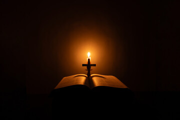 Light candle with holy bible and cross or crucifix on old wooden background in church.Candlelight and open book on vintage wood table christianity study and reading in home.Concept of christ religion