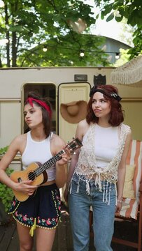 Two guitar-playing hippie girls harmonizing in song.