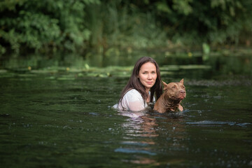 A young beautiful girl swims in the river in a place with pit bull terriers.
