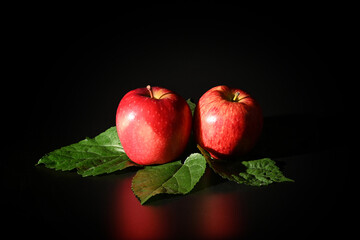 Close-up of red apples on green leaves isolated on black background