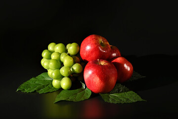 Red apples and green grapes on black background