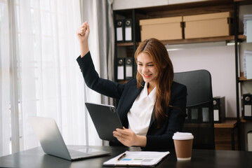 Young attractive Asian woman smiling thinking planning writing in notebook, tablet and laptop working from home at office .