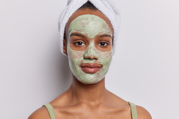 Beauty and cosmetology. Indoor shot of young cheerful European woman standing isolated in centre on white background looking straight at camera applying clay face mask doing skin care procedure