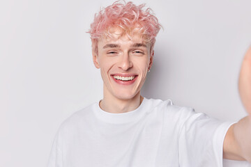 Happy young smiling broadly pink haired gender fluid European male standing isolated on white background wearing casual tshirt belongs to lg by society making selfie or taking photo keeps good shape