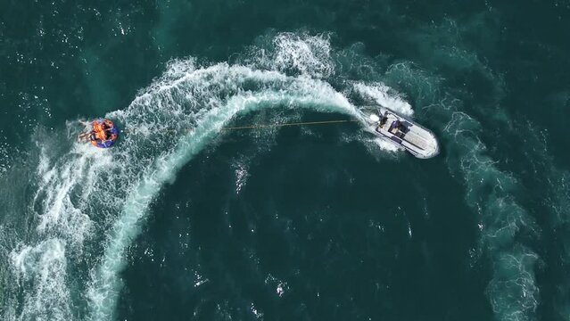 Men riding inflatable donut behind speedboat in the sea, drone view of extreme inflatable donut riding