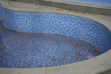bottom of dirty leaking swimming pool removing water so the pool can be repaired.  blue tiled of...