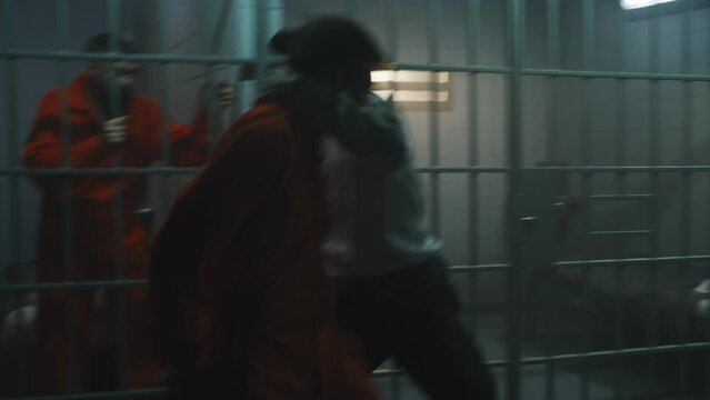Prisoner in orange uniform fights with jailer. Another criminal strangles prison officer and removes handcuffs from cellmate. Escape from jail. Fighting in detention center or correctional facility.