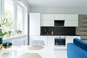 Interior of studio apartment with new white furniture of kitchen, table and chairs. Room with window and modern design.