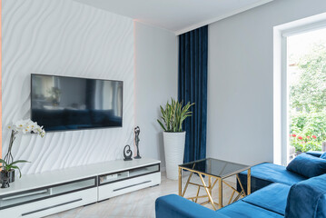 Luxurious living room with navy blue sofa and tv on the design white wall. Modern room in apartment with window in hotel.