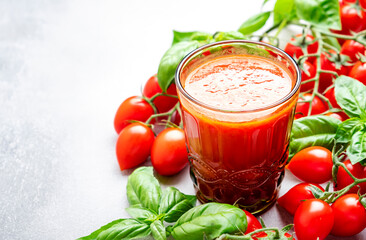Freshly squeezed tomato juice in a glass and red cherry tomatoes on branches with green basil on...
