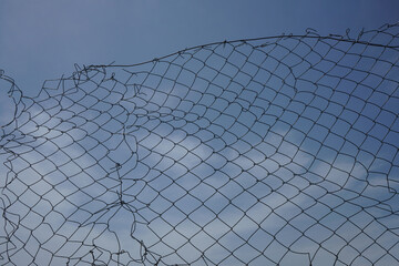 Old rusty damaged wire mesh with sky background, freedom concept, copy space. Opening in metallic...