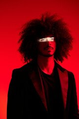 Fashion portrait of a man with curly hair on a red background, multinational, colored light, trendy, modern concept.