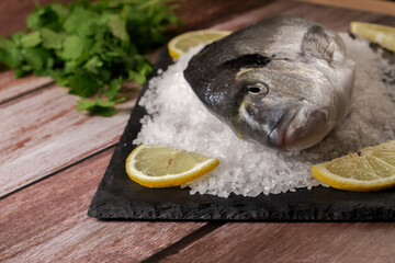fresh sea bream on a slate with salt and lemon on a wooden table with a copy space