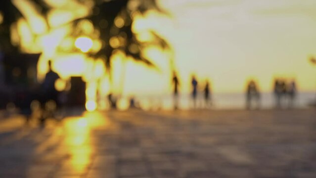 Blurred background of park at the beach with sidewalk and people exercising in the morning, in the golden sun.