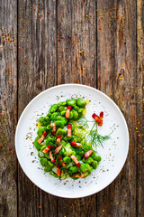 Broad beans with garlic, dill and bacon on wooden table, top view
