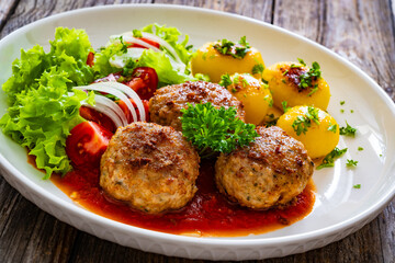 Seared pork meatballs in tomato sauce with fried potatoes  and fresh vegetables on wooden table
