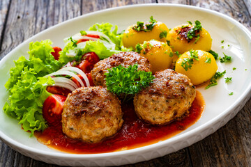 Seared pork meatballs in tomato sauce with fried potatoes  and fresh vegetables on wooden table

