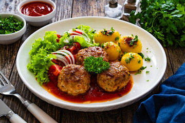 Seared pork meatballs in tomato sauce with fried potatoes  and fresh vegetables on wooden table
