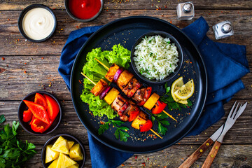 Meat skewers - grilled meat and pineapple with white rice and vegetables on wooden background
