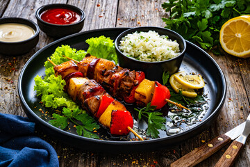 Meat skewers - grilled meat and pineapple with white rice and vegetables on wooden background
