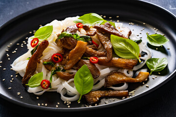 Asian food - fried soy sauce oyster mushrooms with rice noodles on black table
